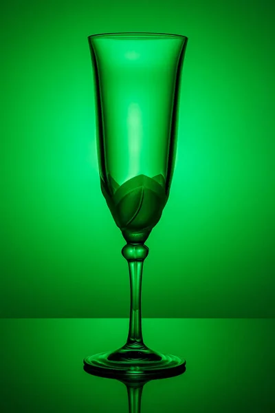 Copo de champanhe transparente vazio em uma perna alta fina com reflexão em uma superfície brilhante escura em luz de fundo verde — Fotografia de Stock