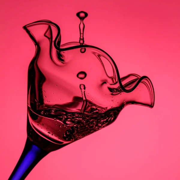 Copa de cóctel inclinada en pierna azul con chorro de agua congelada y salpicaduras de primer plano en luz de fondo rosa. Detener fotografía en movimiento — Foto de Stock