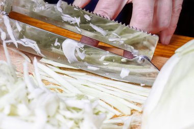 Tahta kesme tahtasındaki lahana parçalamak için taze beyaz lahana yapraklarını bıçakla kesiyor.