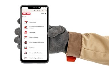 Moskova, Rusya - 25 Mayıs 2020: Akıllı telefon ekranındaki HILTI şirketi web sitesi işçi eli siyah koruyucu eldiven ve beyaz arka planda izole kahverengi üniforma ile yakın plan