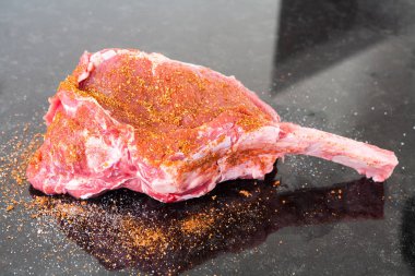 Ham bir parça et baharatlar siyah bir tabloda bir kemik üzerinde