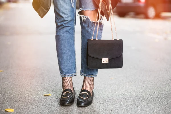 Fall outfit fashion details, young stylish woman wearing ripped jeans and black loafers. fashion blogger holding a trendy black purse with a golden chain. — Stockfoto