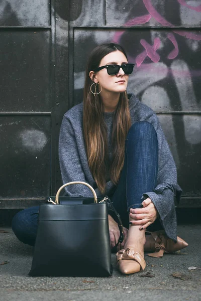 대형된 회색 스웨터, 청바지와 베이 지로 퍼를 착용 하는 세련 된 여자. 도시 여자 블랙 선글라스를 착용 하 고 검은색 유행 핸드백과 함께 포즈. 완벽 한가 옷. — 스톡 사진