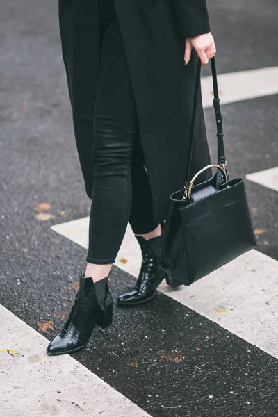 Femme à la mode portant un manteau surdimensionné noir, jeans noirs, chaussures de cheville noires un sac à main noir à la mode . — Photo