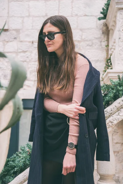 Gyönyörű barna divat blogger pózol az utcán. visel elegáns őszi ruhát, por rózsaszín pulóver, fekete szoknya és egy trendi túlméretezett kabát. meleg fokozat, utcai stílus — Stock Fotó