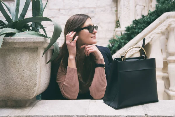 Modedetails. junge Mode-Bloggerin mit trendiger Sonnenbrille und posiert mit einer eleganten schwarzen Handtasche. ideale Herbst Outfit Accessoires. — Stockfoto