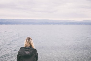 Sahilde yalnız kadın. rüzgarlı bir sonbahar günü denize bakarak üzgün ve endişeli kadın. ideal kitap kapağı.