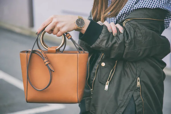 Menutup rincian mode, wanita memegang tas elegan coklatnya. memakai jam tangan hitam dan emas. ideal pakaian musim semi aksesoris .fashion blogger berpose dalam gingham check top dan jaket bomber . — Stok Foto