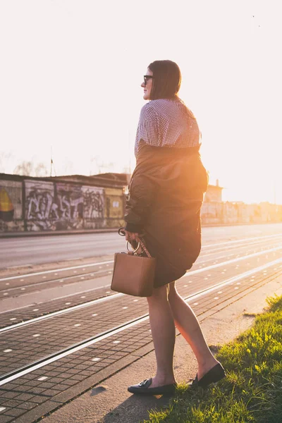 mükemmel bahar moda kıyafet. Pötikareli onay topaç, siyah etek, büyük boy bombardıman ceket, loafer'lar ve kahverengi bir çanta giyen moda kadın. Blogger sokakta günbatımında poz moda.