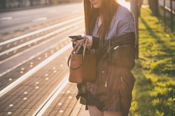 Wanita muda perkotaan menggunakan smartphone-nya di jalan kota saat matahari terbenam. blogger fashion SMS di teleponnya. Wanita bergaya menggunakan ponselnya untuk jejaring sosial. konsep belanja online . — Stok Foto