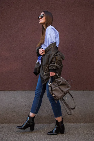 Traje de moda de primavera perfecto. blogger europeo de moda con una blusa de rayas crossover de moda con un nudo frontal, una chaqueta de bombardero, jeans, botas de tobillo y sosteniendo un bolso con estilo . —  Fotos de Stock
