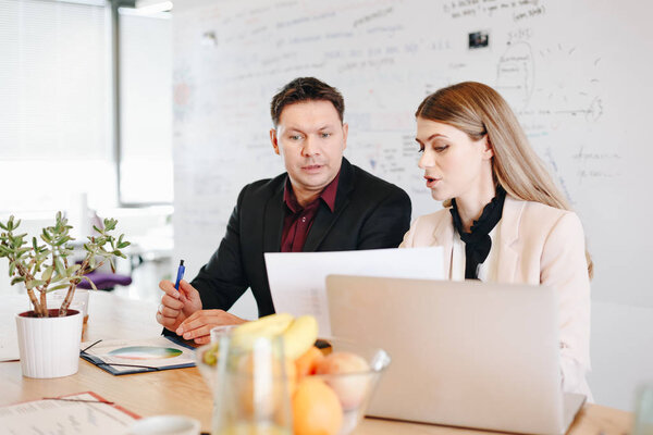 Two coworkers having a discussion in the office. Candid moment, business woman and business man talking about new presentation strategy using graphs and laptop.