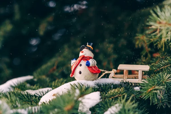 Primo piano decorazione natalizia pupazzo di neve in miniatura con skarf rosso e slitta sul ramo — Foto Stock