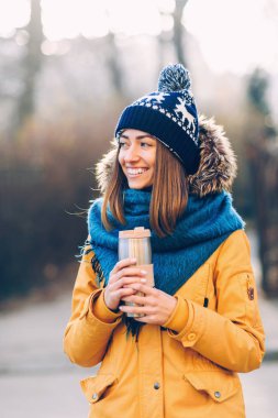 Genç güzel kız sıcak şapka ve atkı thermocup elinde ile sokakta yürürken