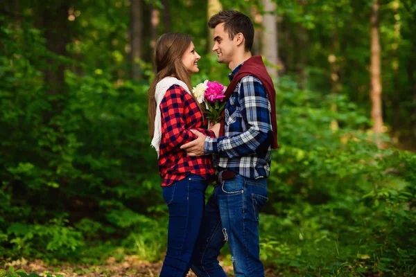 Snygga unga par i skjortor och jeans medan promenader i skogen. En charmig tjej och hennes stiliga pojkvän tittar på varandra. — Stockfoto