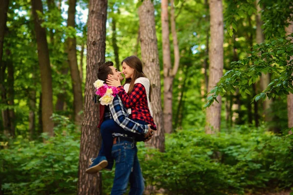 Snygga unga par i skjortor och jeans medan promenader i skogen. En stilig modiga pojkvän håller hennes vackra attraktiva flicka i händerna. — Stockfoto