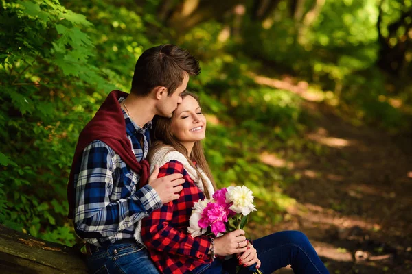 Stylish young couple in shirts and jeans while walking in the forest. A handsome boyfriend kisses his beautiful charming girlfriend on the forehead.