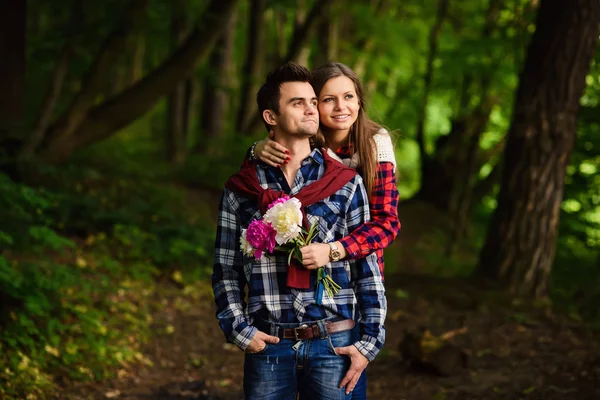 Elegante giovane coppia in camicie e jeans mentre passeggia nel bosco. Bella ragazza affascinante abbraccia il suo bel fidanzato . — Foto Stock