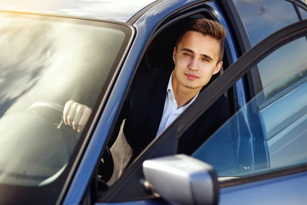 Bonito atraente homem elegante em um terno de negócios dirigindo um carro caro — Fotografia de Stock