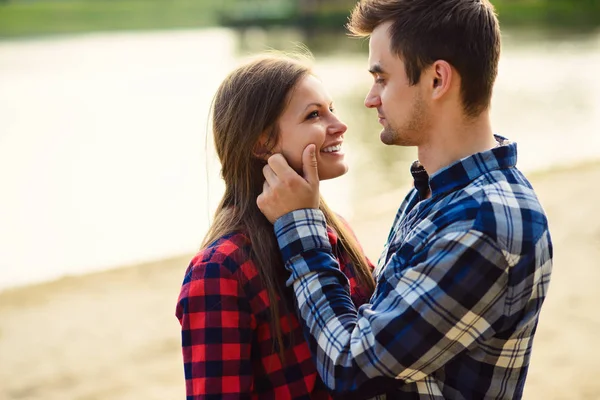 Stylish young couple in shirts and jeans while walking along the lake shore. A beautiful attractive girl and her handsome boyfriend are looking at each other.