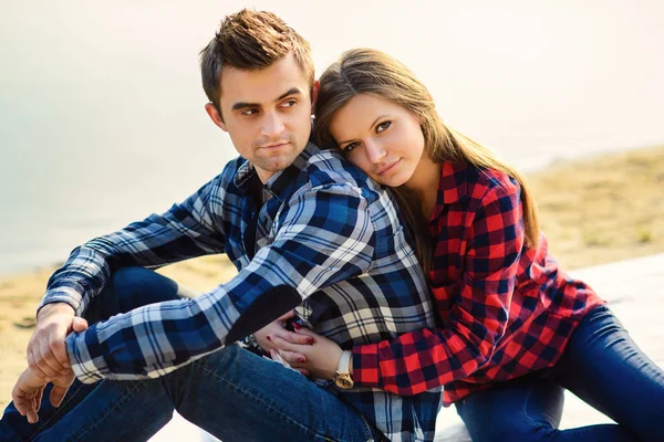 Stylish young couple in shirts and jeans while walking on the shore of a lake. Beautiful charming girl hugs her handsome boyfriend. Close up portrait.