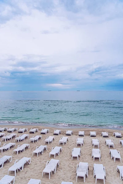 Sillas blancas en la playa de arena contra el fondo del mar y el cielo nublado noche — Foto de Stock