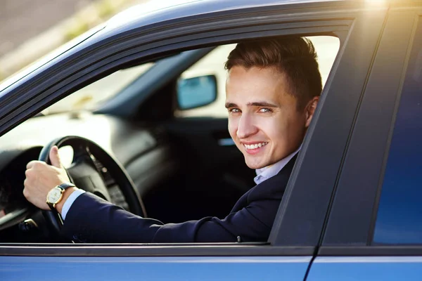 Attraente bell'uomo sorridente in un abito da lavoro alla guida di una macchina costosa — Foto Stock