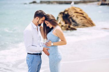 Seven çift sahilde hamile kadının karnında sevgi ve bakım arka planda kayalar ve deniz güneşli bir günde dokunmadan.