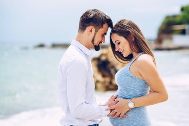 Seven çift sahilde hamile kadının karnında sevgi ve bakım arka planda kayalar ve deniz güneşli bir günde dokunmadan.