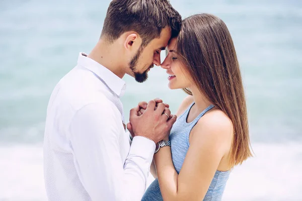 Una hermosa mujer embarazada en un vestido azul y su valiente y guapo marido en una camisa y pantalones azules se inclinaron el uno al otro sobre el fondo del mar . — Foto de Stock