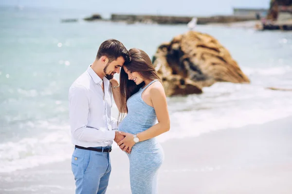 Coppia amorevole sulla spiaggia toccando pancia della donna incinta con amore e cura sullo sfondo di rocce e mare nella giornata di sole . — Foto Stock