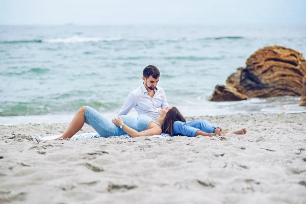 Mulher grávida bonita e seu homem respeitável encostados uns contra os outros e sentados na praia. Adorável jovem casal . — Fotografia de Stock