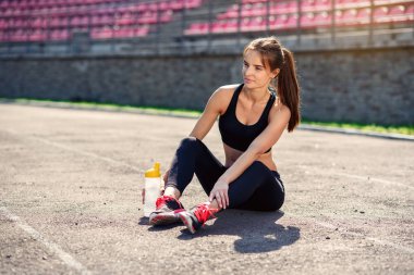 Şişe su ve enerji ile oturan yorgun fitness kız içki stadyumun eğitimden sonra koşu bandı üzerinde. Sporcu kız eğitim sırasında bir mola. Spor, sağlık kavramı.