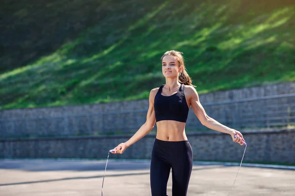 Athlete woman jumping with skipping rope at stadium. Active fitness female doing exercises outdoor. Fitness concept. Healthy lifestyle.