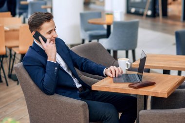 Onun çalışma alanı laptop, m-cüzdan ve defter ile smartphone konuşan başarılı bir iş adamı. Forex cryptocurrency ticaret, iş kavramı. Elektronik sanal para yatırım.