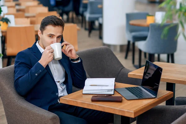 Overworked businessman have coffee break and speaking on smartphone. Cryptocurrency mining. Gold and silver bitcoin coin. Electronic virtual money investment. Selective focus.