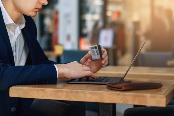 Man holding in hand a credit card and using laptop for online shopping. Web banking and international network payment. Online payment concept.