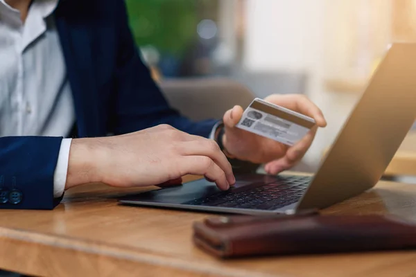 Man holding in hand a credit card and using laptop for online shopping. Web banking and international network payment. Online payment concept.