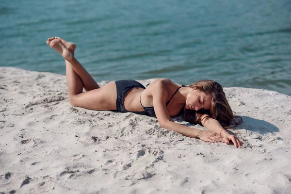 可爱的运动女孩 穿着黑色泳装在夏日沙滩上 一个晒黑的女孩在海滩上沐浴阳光 — 图库照片