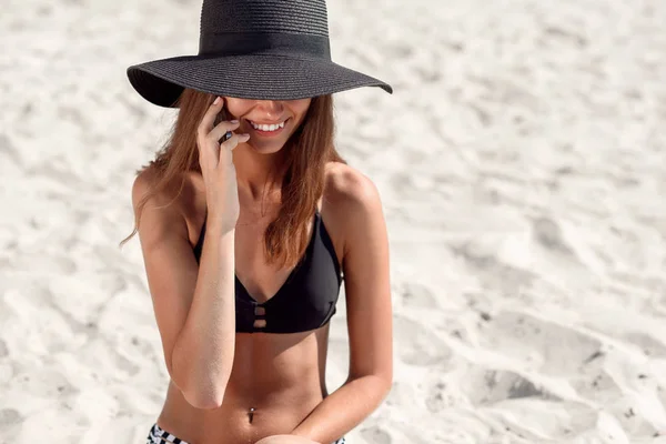 迷人的女孩在海滩上放松 用智能手机聊天 迷人的女孩戴着夏天的帽子和性感的比基尼 — 图库照片