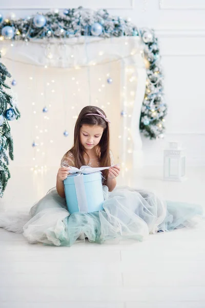 Menina bonita sentada perto da árvore de Natal dentro de casa . — Fotografia de Stock