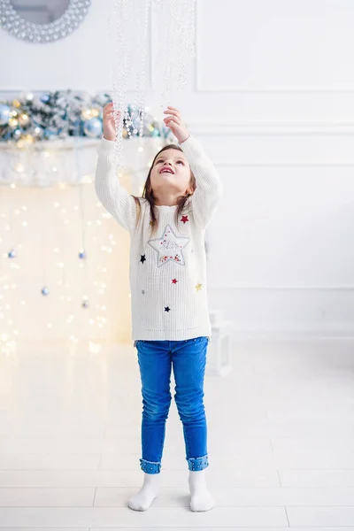 Menina bonita sentada perto da árvore de Natal dentro de casa . — Fotografia de Stock