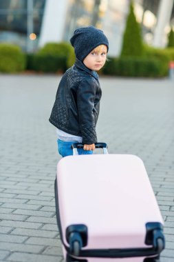 Şirin küçük gezgin kız pembe bavulunu havaalanına doğru çekiyor..