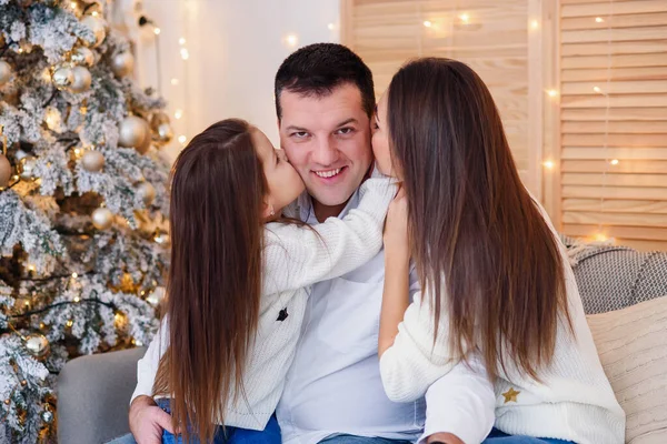 Young mom, father, and their little daughter lovely sitting near Christmas tree on sofa.