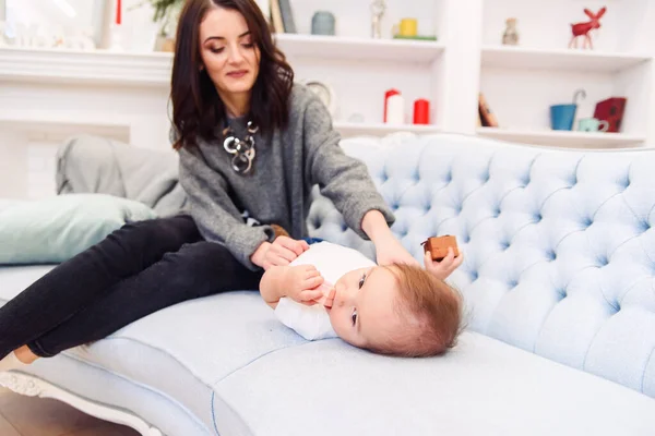 Leuke peuter ligt op de blauwe bank en gelukkig jong mama kneden zijn benen en maakt hem gelukkig. — Stockfoto