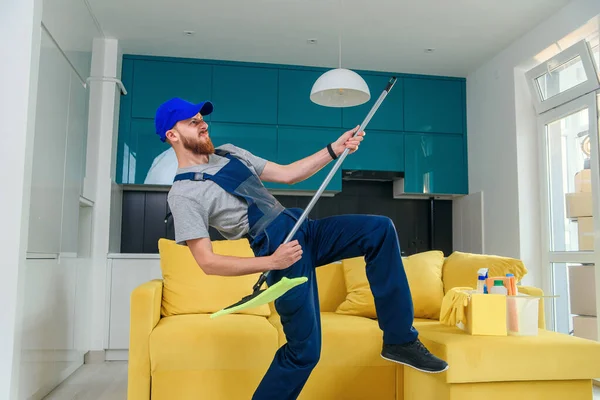 Funny picture of male cleaning worker in special clothes playing with a mop as a guitar in the kitchen — Stock Photo, Image