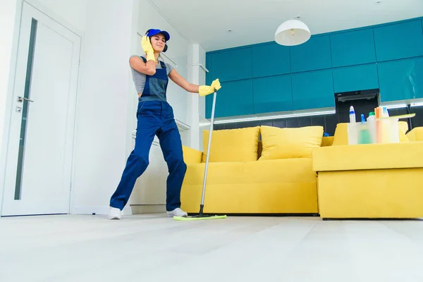 Caucasian woman as a professional cleaner in headphones cleaning floor with mop and listens to music at home. — Stock Photo, Image