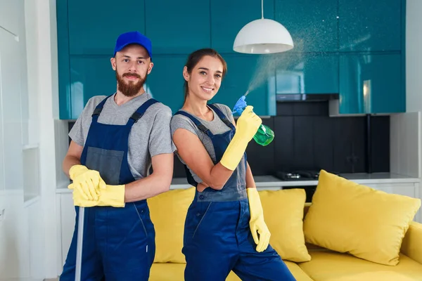 Een paar professionele schoonmakers verblijven samen in de hedendaagse keuken met detergentia. Concept schoonmaakdiensten. — Stockfoto