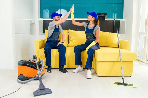 Tevreden schoonmakers in blauwe uniformen geven elkaar high five en blijven de vloer schoonmaken in de keuken. — Stockfoto