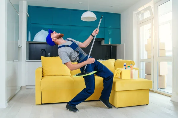 Funny picture of male cleaning worker in special clothes playing with a mop as a guitar in the kitchen — Stock Photo, Image